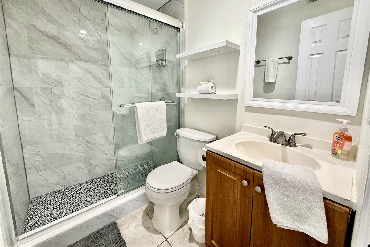 Modern and efficient, this light-filled bathroom includes a curved glass shower with spa-style amenities, plush white towels, and a window that welcomes natural light while maintaining privacy.