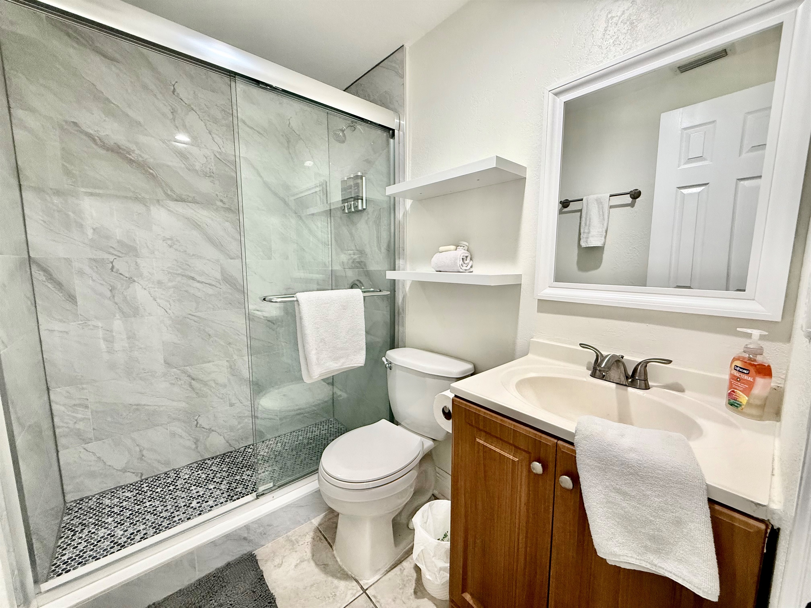 Modern and efficient, this light-filled bathroom includes a curved glass shower with spa-style amenities, plush white towels, and a window that welcomes natural light while maintaining privacy.
