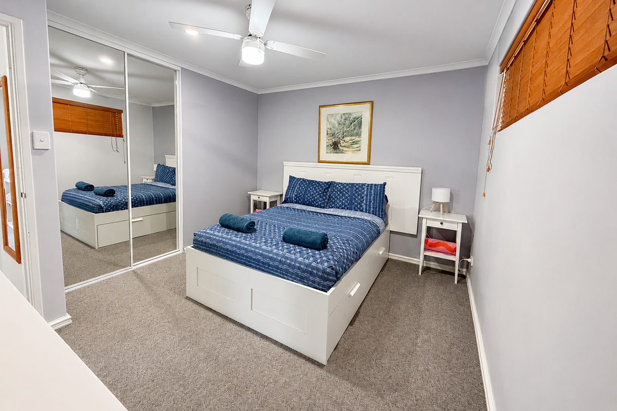 Soft blue bedding, timber blinds and mirrored storage give this Josh’s Sea Breeze bedroom a clean, relaxed feel after days by the water.