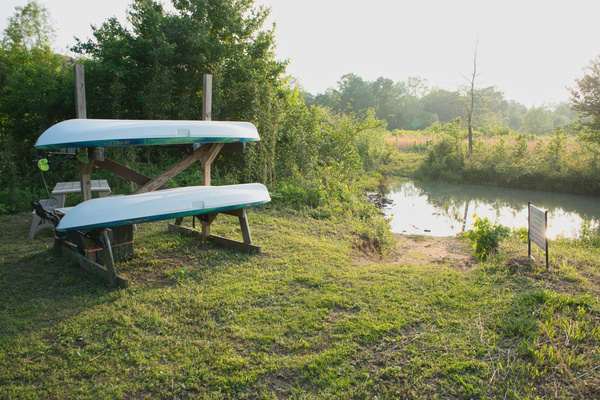 Guest-use kayaks are stored near the waterfront access area that includes a picnic table that converts to benches and life jackets, with entry point down to the water.