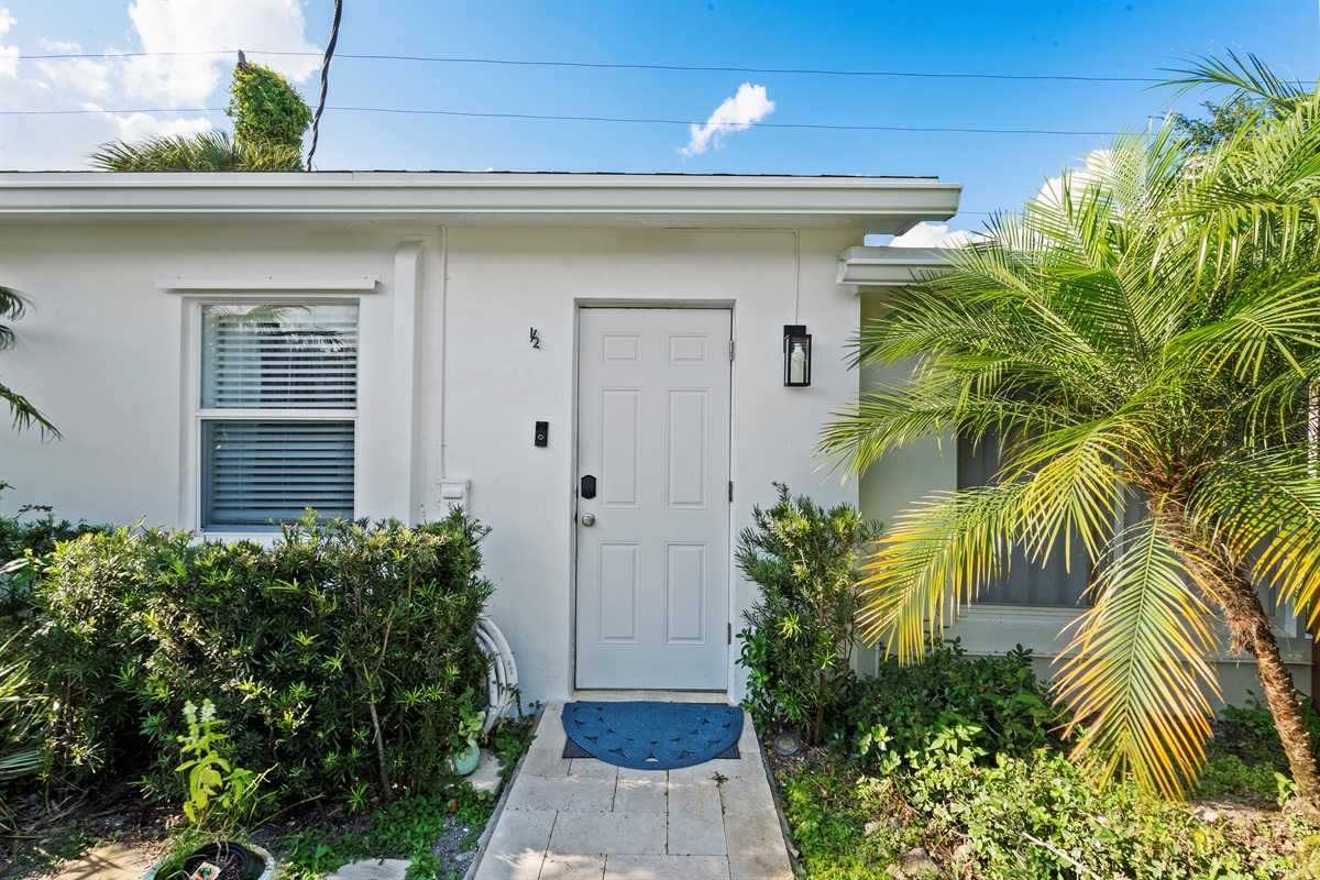 Charming cottage entrance tucked among lush palm trees and greenery.