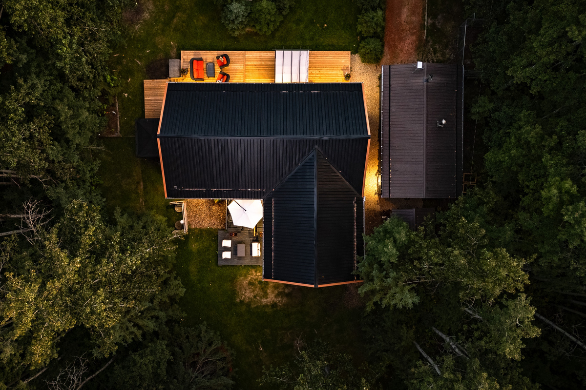 A bird's-eye view shows Aspen Acre tucked into the trees, with the cabin, decks, and outdoor spaces glowing warmly after dark.