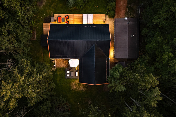 A bird's-eye view shows Aspen Acre tucked into the trees, with the cabin, decks, and outdoor spaces glowing warmly after dark.