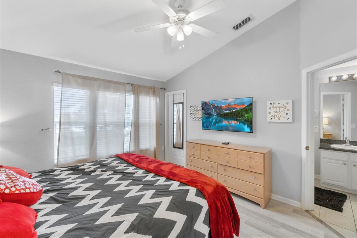 - Sun filled bedroom with king bed, large windows, and soft sheer curtains  
- TV and dresser provide in room entertainment and storage options  
- Connected ensuite and ceiling fan create a comfortable, relaxing escape