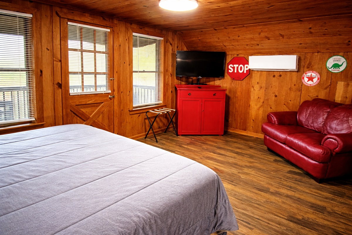 Cozy cabin bedroom with plush bedding, a comfy leather loveseat, and TV — the perfect spot to relax after a day in the mountains.