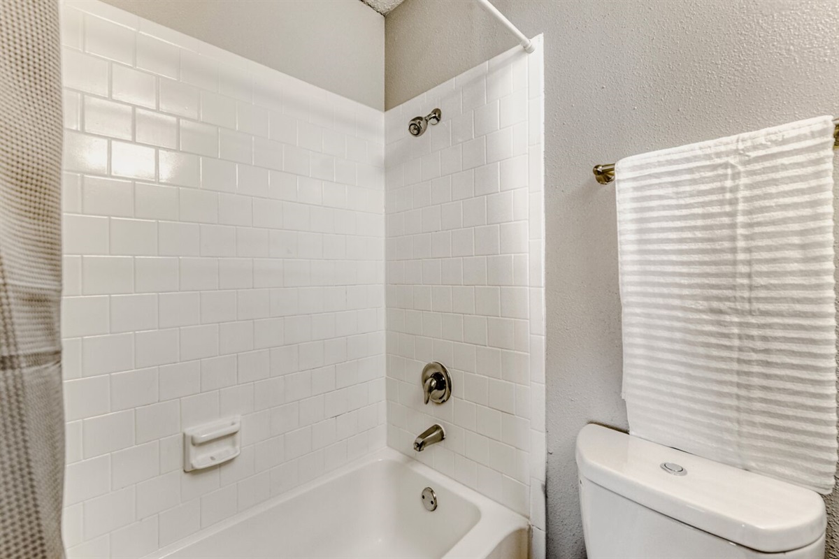 Simple bathroom with clean white tiles and a classic bathtub-shower combo.
