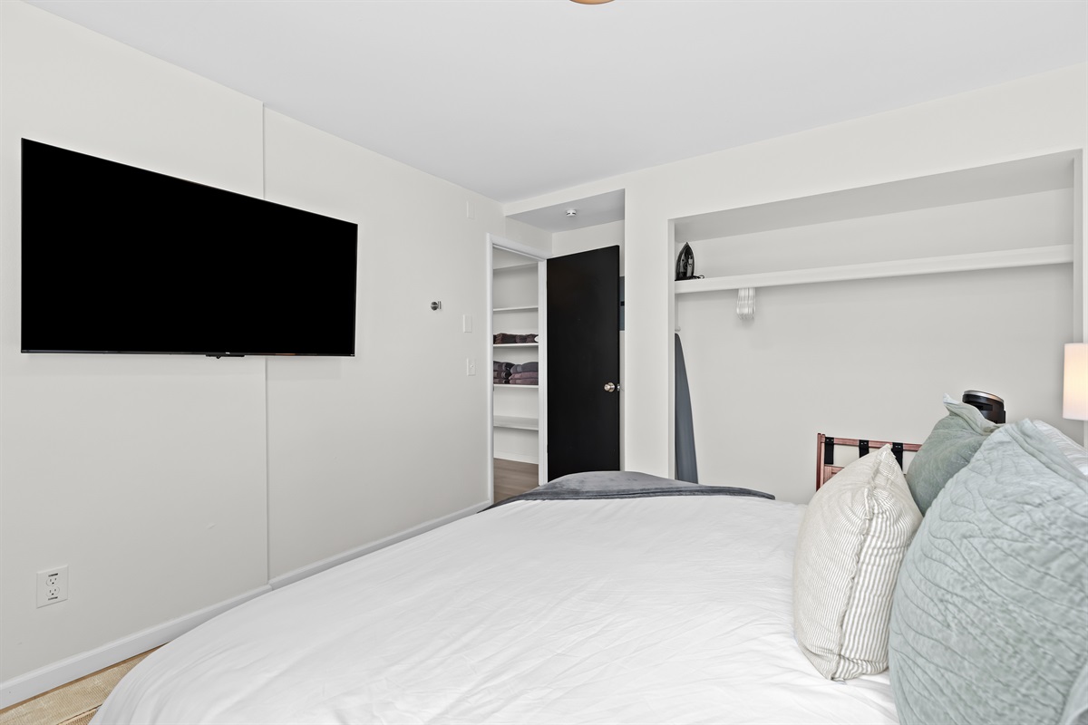 Rest easy in this calming bedroom featuring a mounted smart TV, open shelving, and plenty of extra blankets for your comfort.