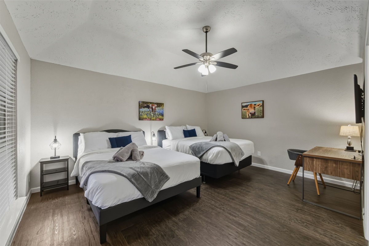 Spacious master suite with two queen beds, TV, and dedicated workstation.