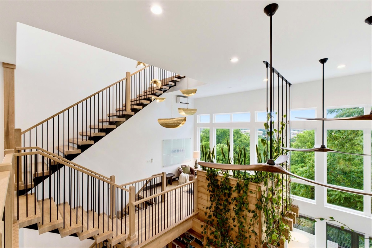 Sun-drenched stairwell w/ trailing plants, wood steps & walls of glass bringing the outside in.
