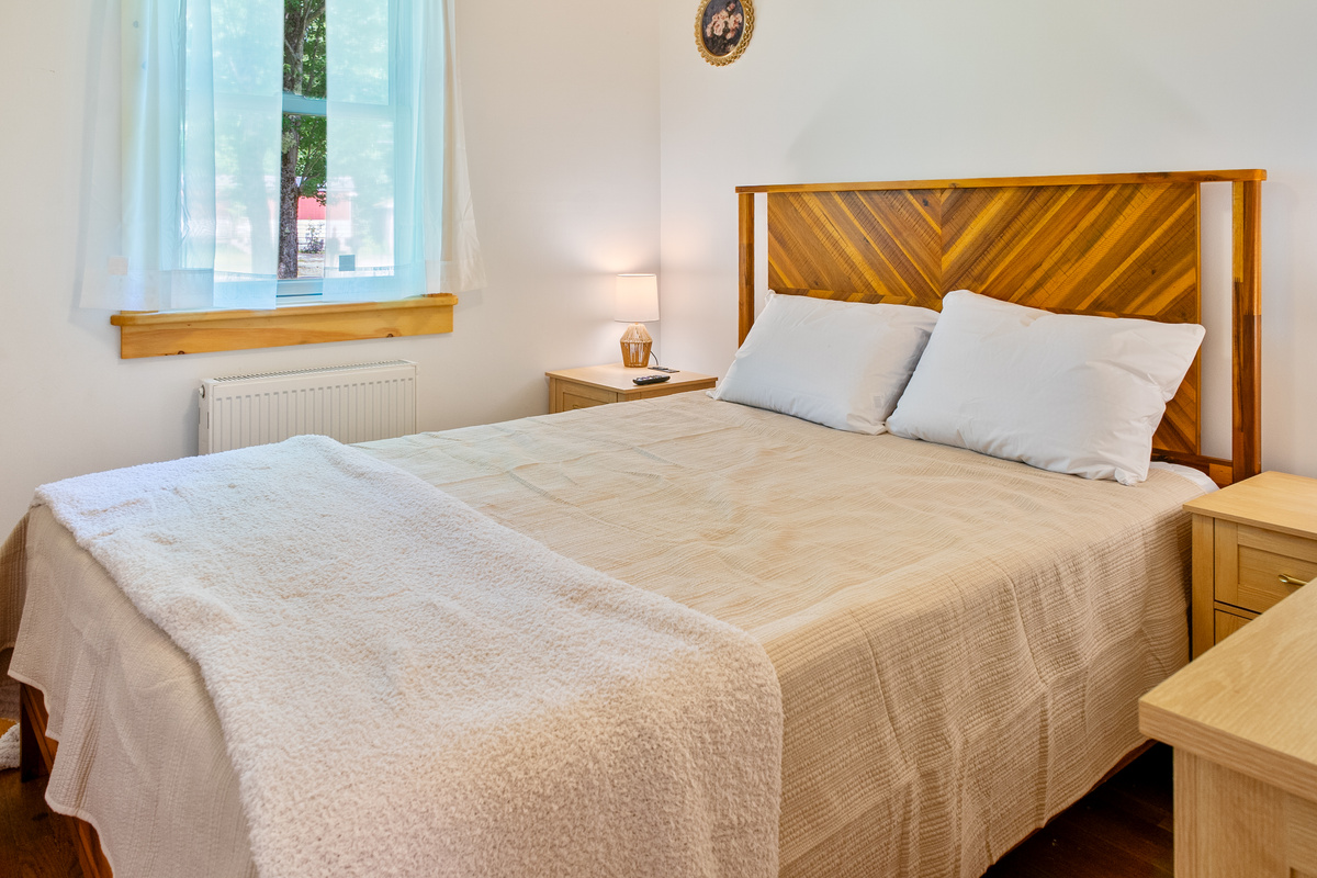 Sleep on a plush memory foam mattress in the queen guest bedroom, complete with dual wooden nightstands featuring integrated charging ports. This closer perspective showcases the natural sunlight filtering through the nearby window.