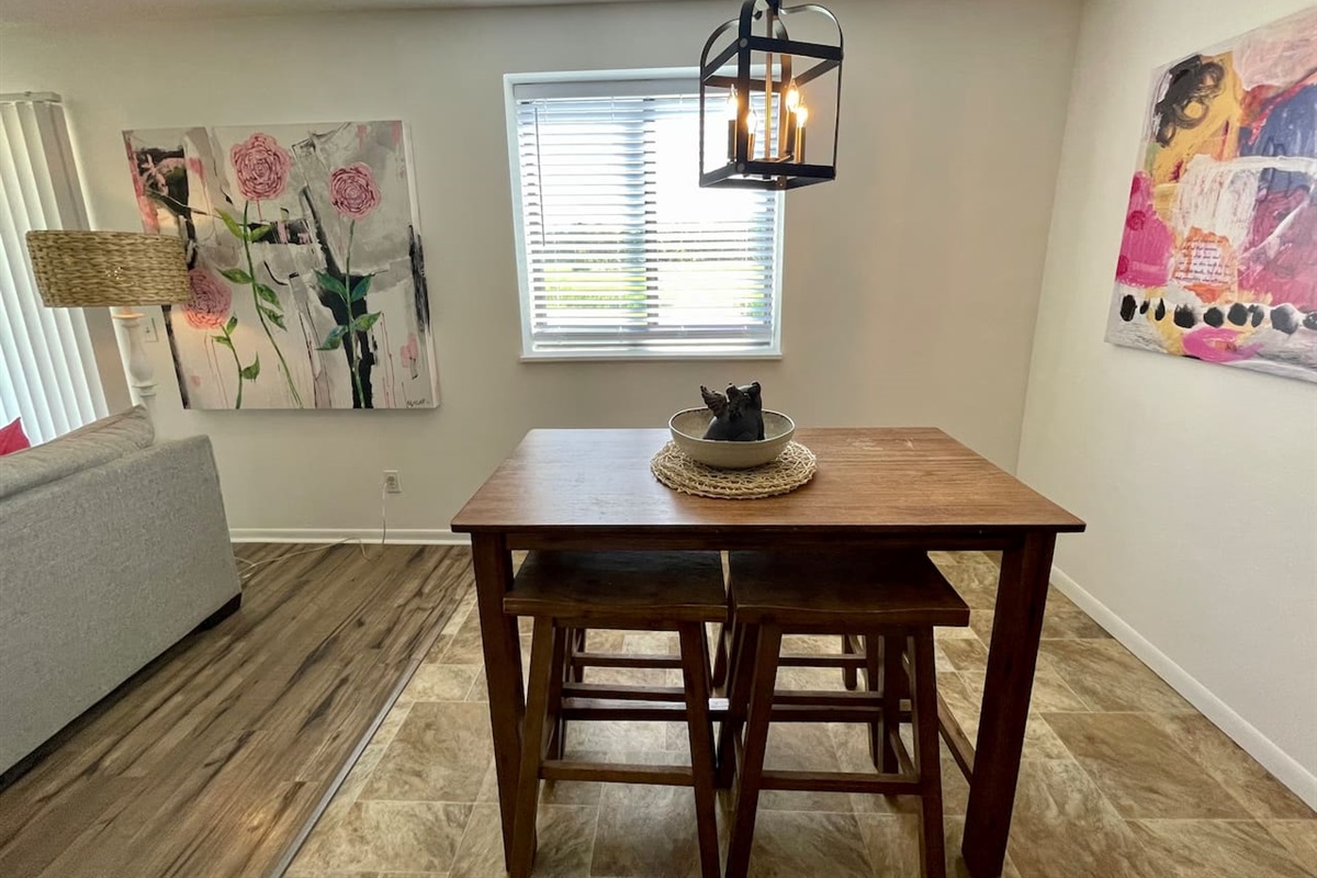 Bright dining area with modern art, natural light, and a cozy wood table for four. A charming lantern-style light fixture adds character, making it a perfect space for meals, board games, or enjoying your morning coffee.