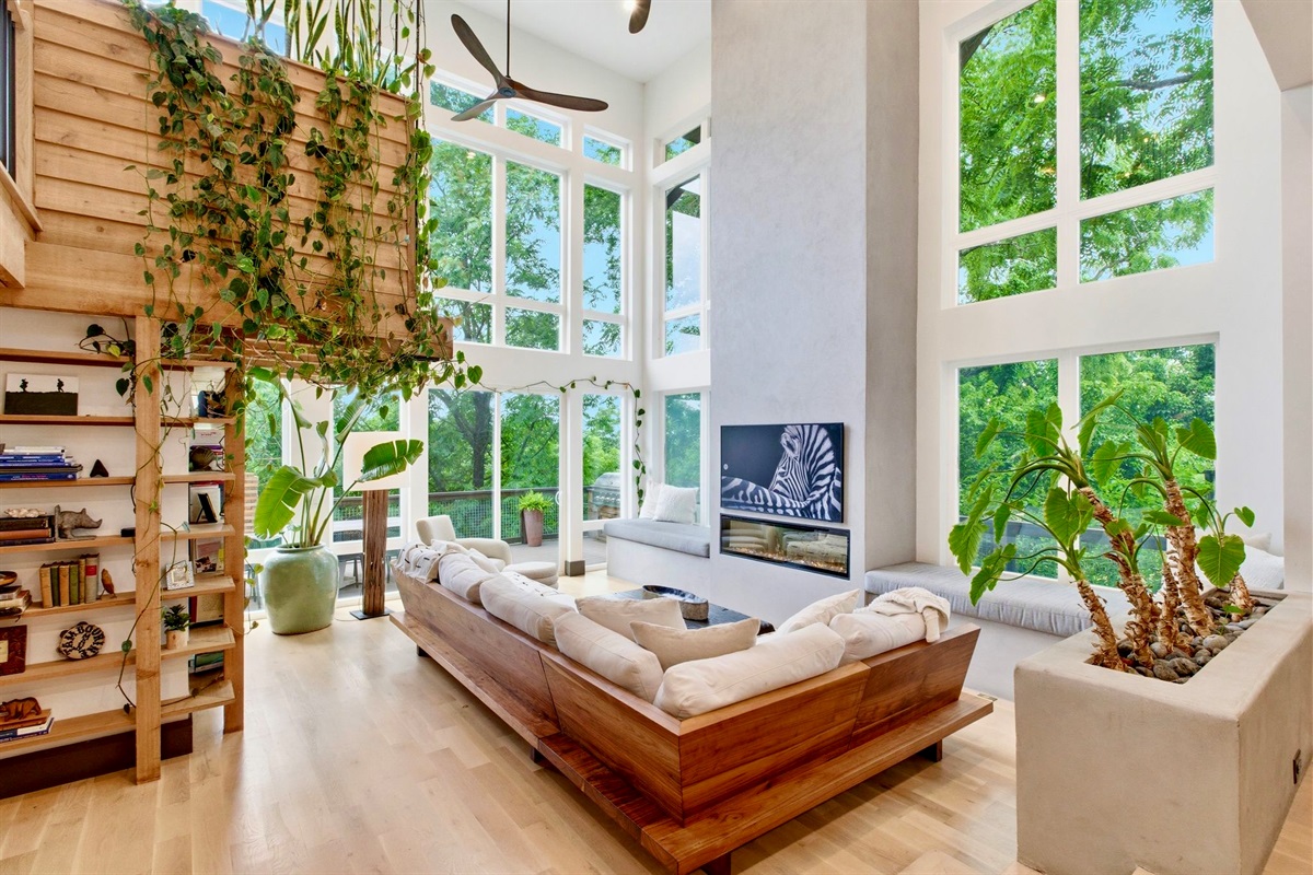 Plant-filled sitting room w/ floor-to-ceiling windows, warm wood accents & a sun-soaked sofa nook.
