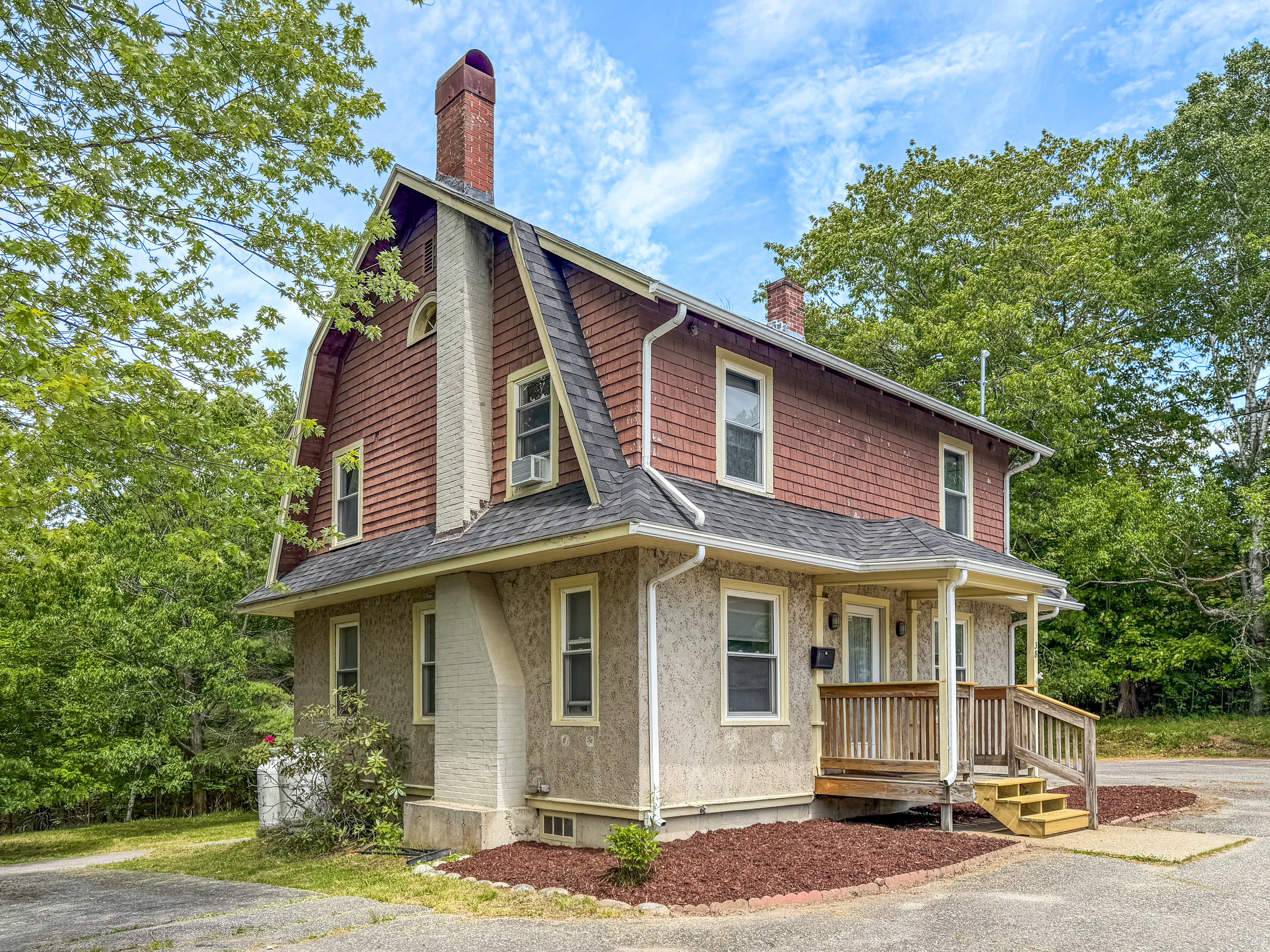 This architectural view highlights the historic stone-pressed stucco siding, brick chimney, and gambrel roof. An upper window AC unit ensures climate control, verifying functional modern comfort at this private Downeast vacation home rental.