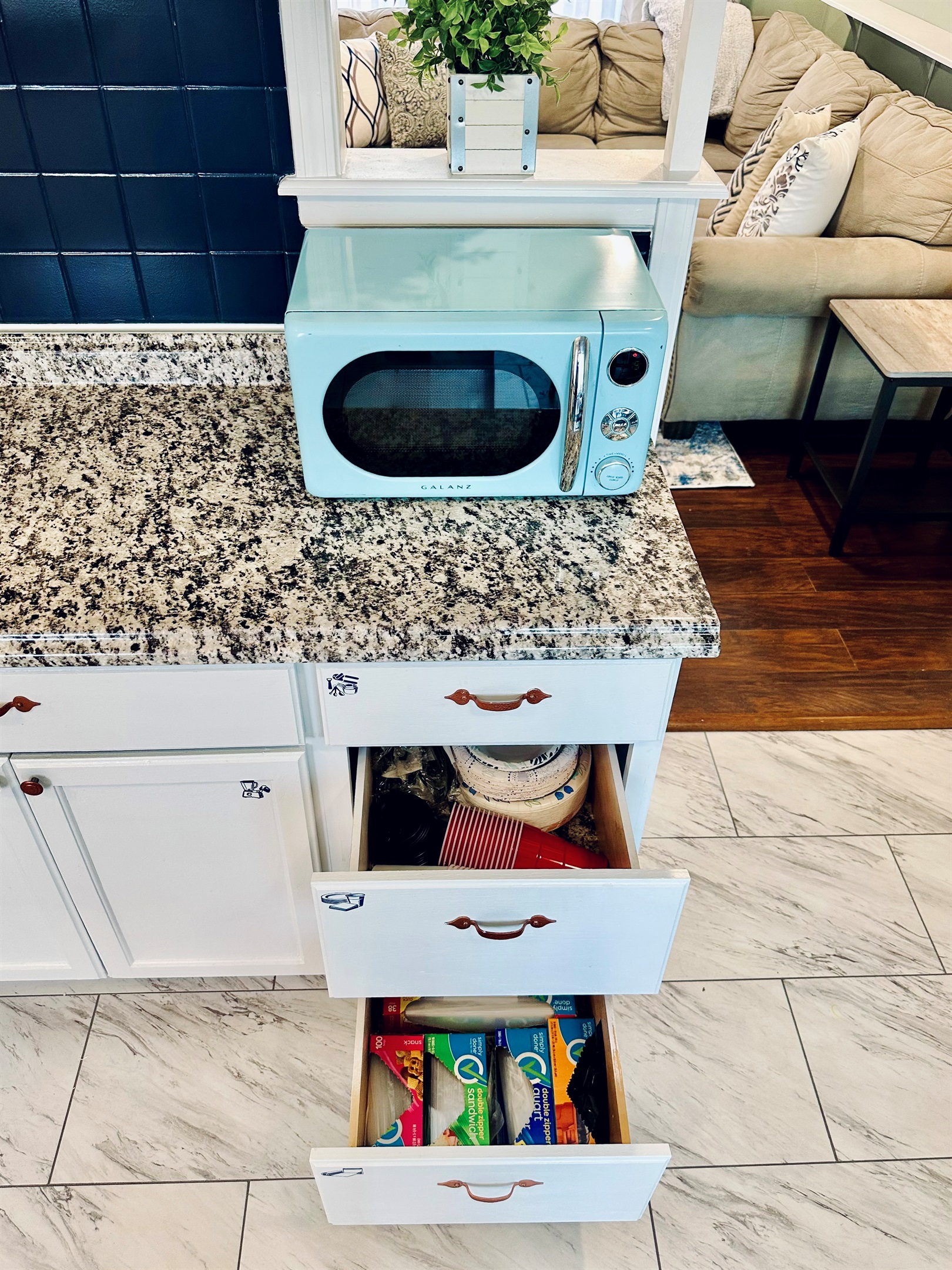 Kitchen drawers organized with paper plates, bowls, disposable cups, utensils, and napkins, along with food storage bags, aluminum foil, plastic wrap, wax paper, and trash bags—convenient extras for longer stays.