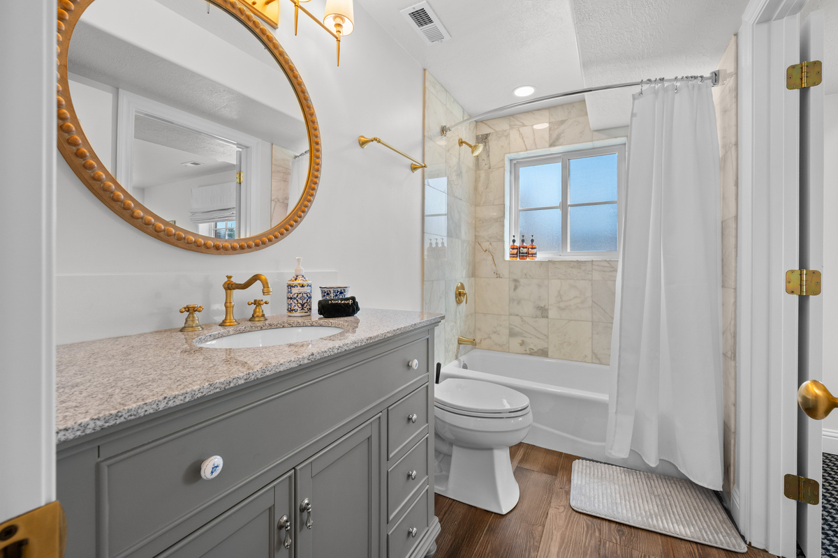A round statement mirror, warm details, and tile bring a refined, timeless feel to this well-appointed bathroom.