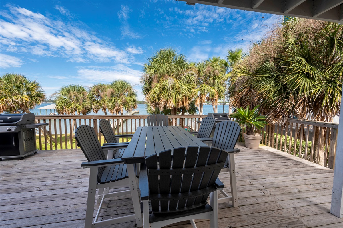 Outdoor deck with a BBQ grill, lush palm trees, Lagoon views, and a serene dining setup for a relaxing feel.
