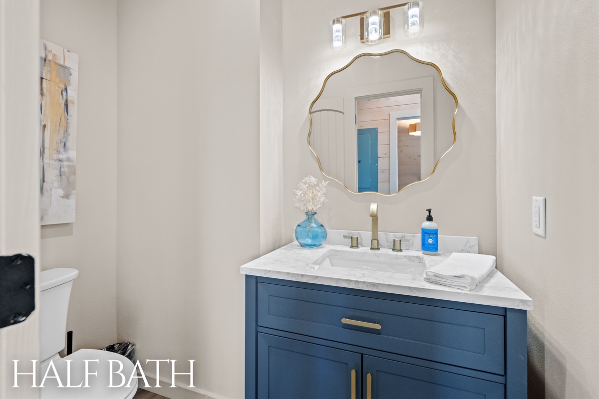 Half bath with farmhouse vanity and gold-framed mirror.
