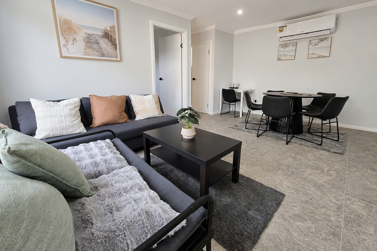 Matilda’s Urban Escape opens into a combined living and dining area with lounge seating, a round dining table and light grey tiled flooring.