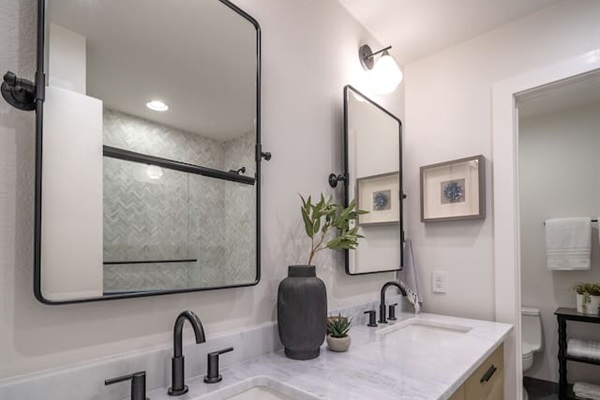 Wide view of the shared hallway bathroom showcasing the double-sink vanity, ample counter space, and a private water closet. Shampoo, conditioner, body wash, and plush towels are provided for guest use.