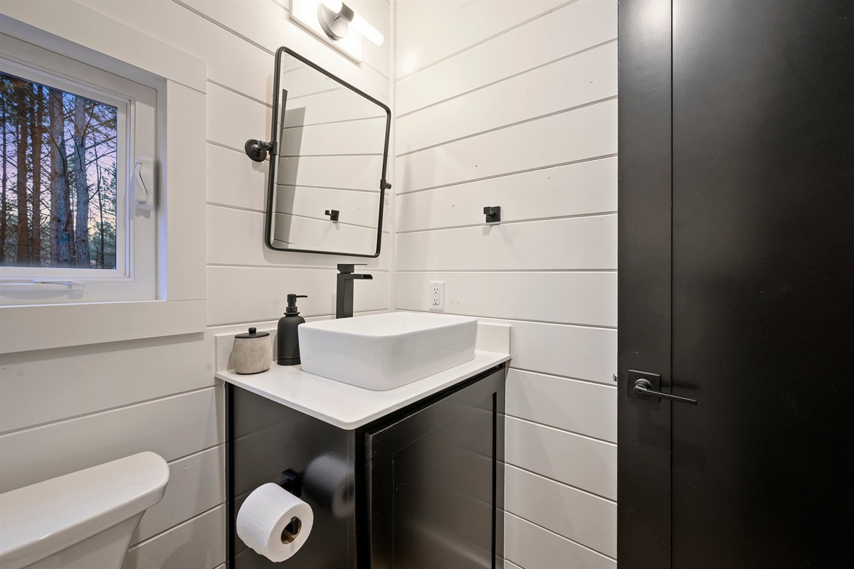 This stylish guest bathroom features modern finishes, a sleek vanity, and charming woodland views.