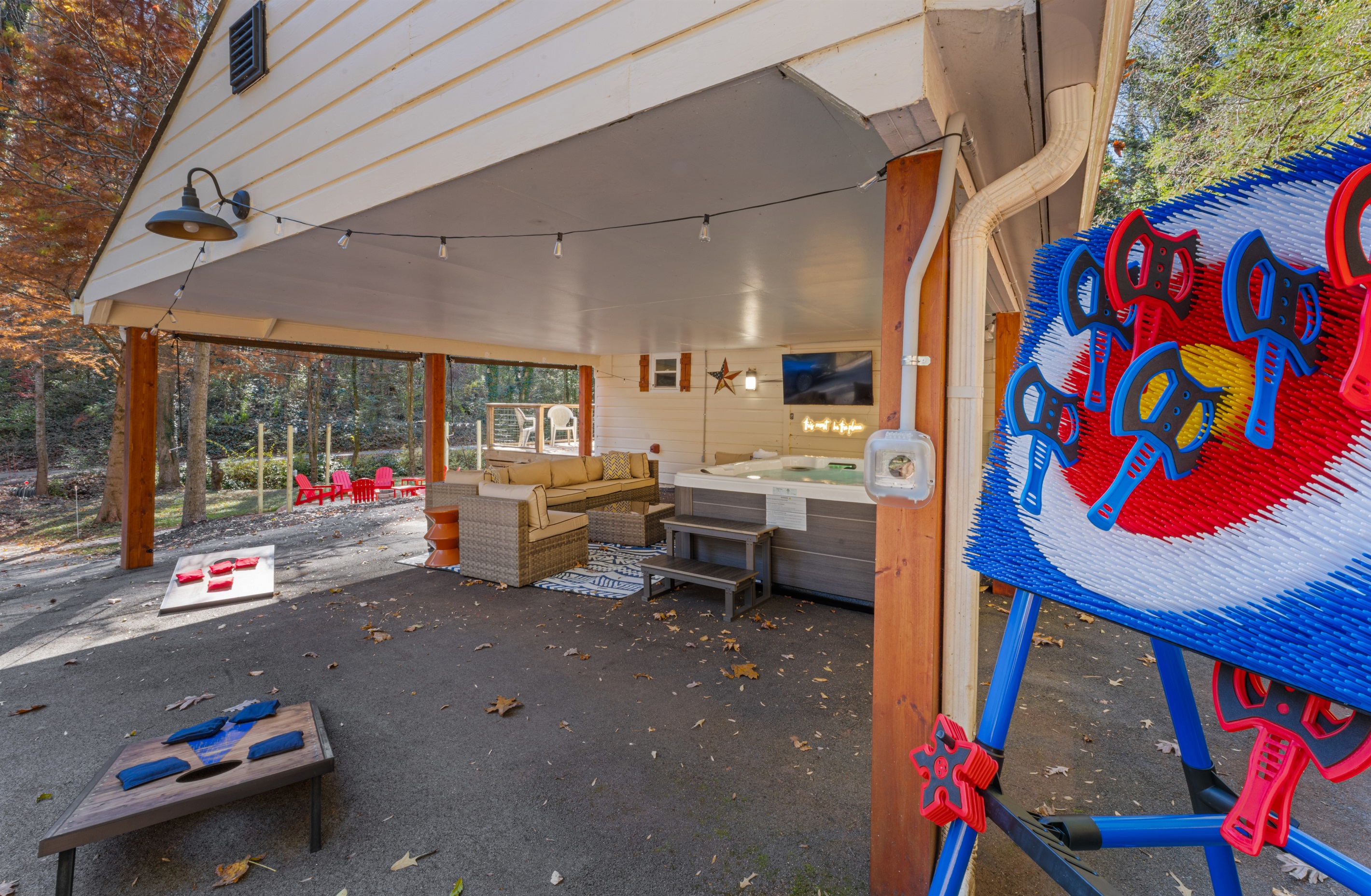 Covered outdoor hangout with hot tub, big-screen TV, lounge seating, and lawn games — perfect for enjoying the fresh air and forest views.