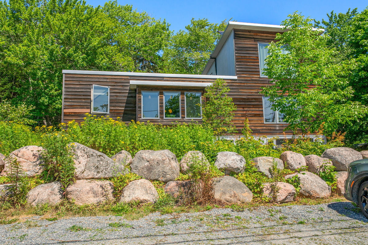 Rising dramatically above natural stone hardscaping, "The Crag" showcases bold vertical design nestled in dense forest canopy. A modern retreat engineered to mirror its mountain setting in Otter Creek, just steps from Acadia's trail network.