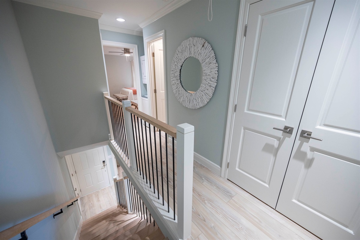 Modern hallway with stylish decor, round mirror, white doors, and a sleek staircase.
