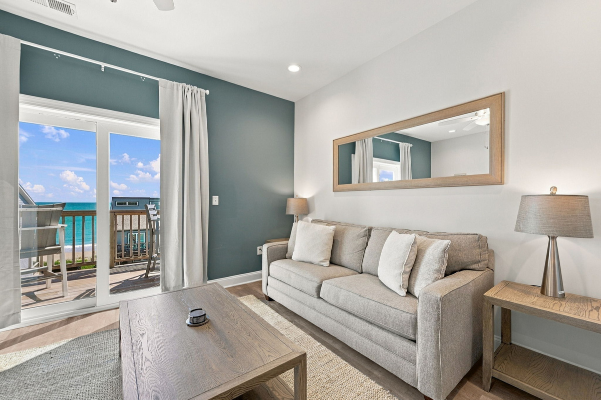 Cozy seating area featuring a neutral sofa, wood coffee table, teal accent wall, and sliding glass doors leading out to a private oceanfront balcony.   