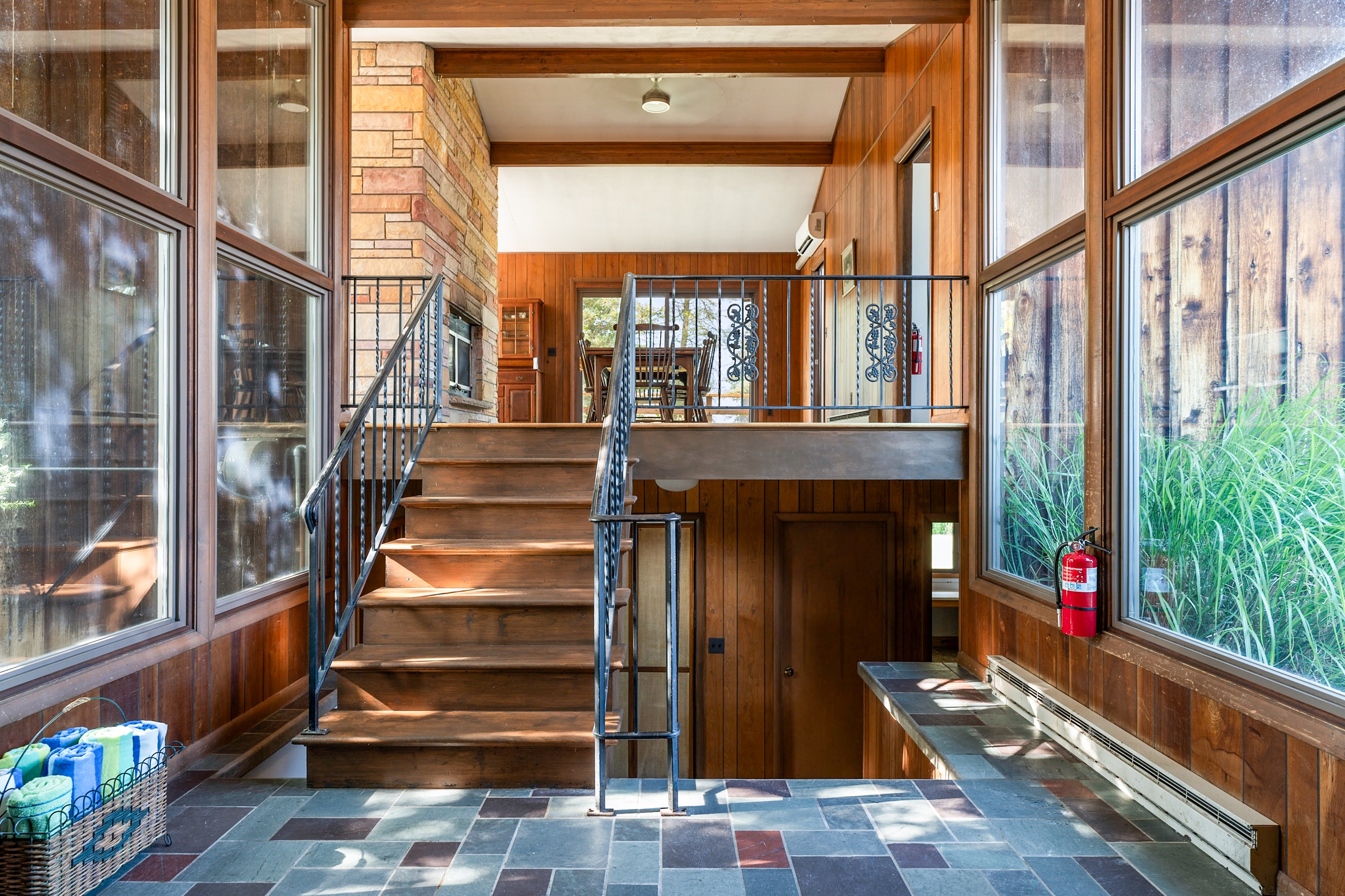 Bright and airy entryway with floor-to-ceiling windows, wood accents, and open stairway leading into the main living area.