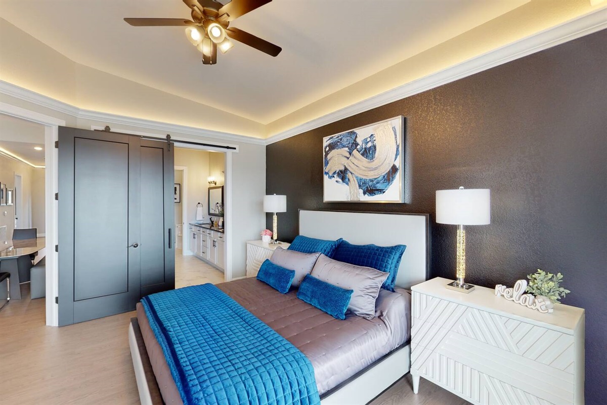 Master bedroom with modern decor, King size bed, private ensuite bathroom, large flat screen tv, surround sound system, ceiling fan, soffit lighting, sliding glass door, and access to the outdoor patio deck.