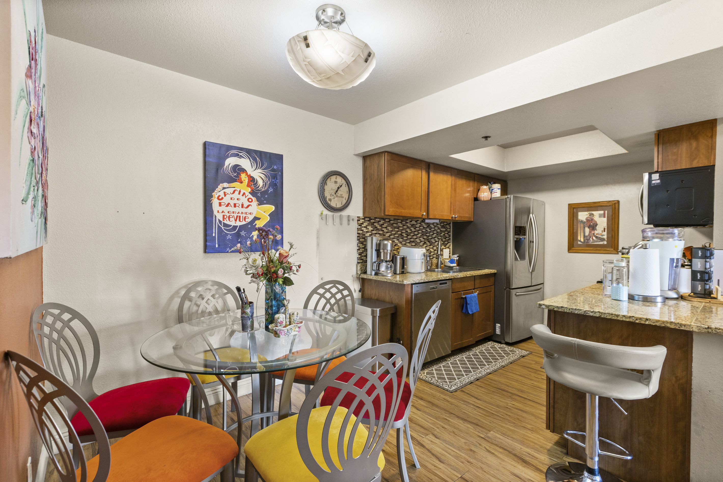 Dining area with colorful chairs, glass table seating, and the kitchen right beside it for easy meals.
