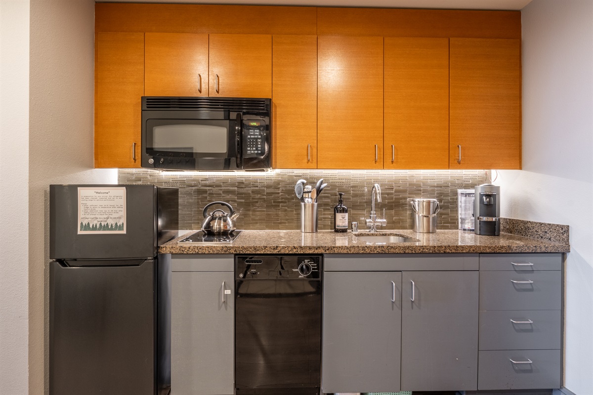 The galley kitchen includes an upgraded, larger refrigerator with a true freezer, along with a dishwasher, microwave, and two-burner cooktop—practical amenities that make everyday meals easier.