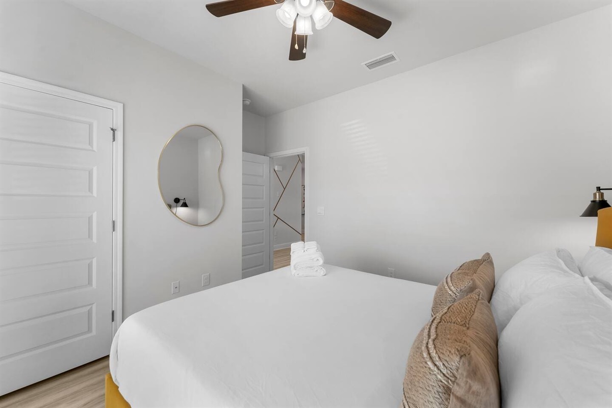 Well-appointed bedroom with cozy lighting, decorative art, a ceiling fan, and a mirror.