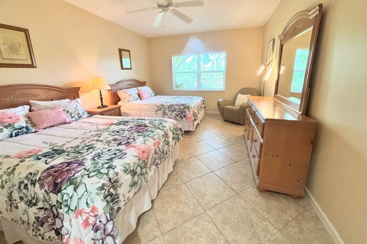 Spacious bedroom with two beds, ceiling fan, dresser storage, and natural light.