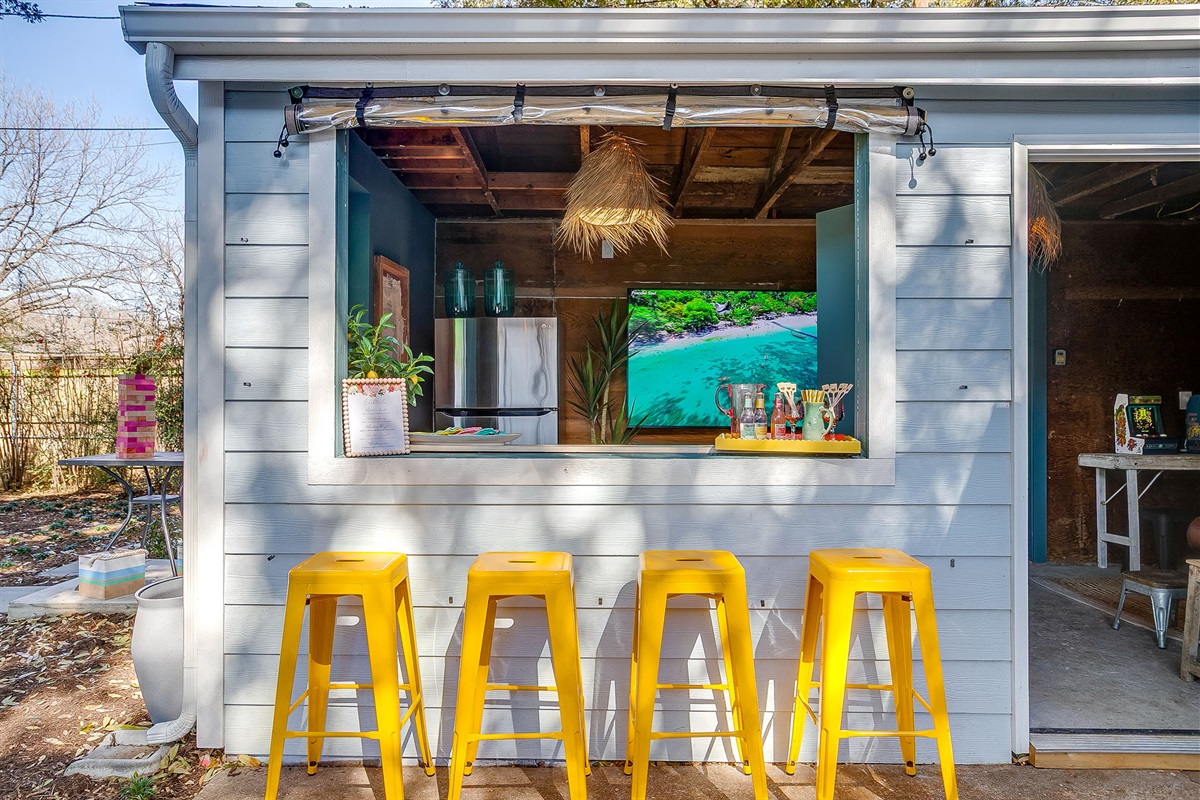Game room bar with secondary fridge and large TV. 