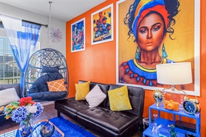 Relax in a colorful, art-filled living room that blends comfort with cultural flair, featuring striking wall art, bold orange accents, and luxurious leather couches for a truly unique experience