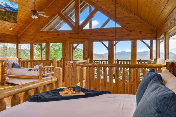 Upper level king suite — soaring A-frame skylights, wraparound Smoky Mountain views, private deck access, Smart TV, and a trundle bed that sleeps two more. Waking up here is the whole point.