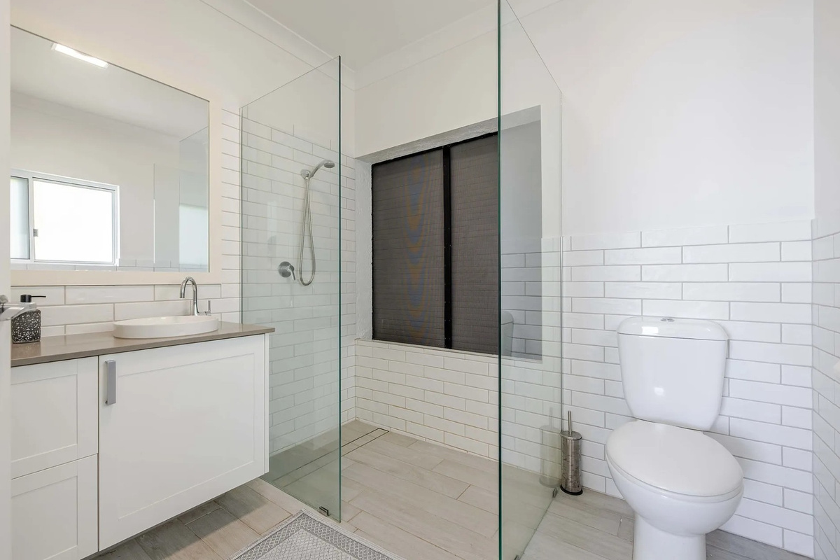 This bathroom includes a glass-screened shower, vanity storage, large mirror and white subway tiling for a clean, practical layout.