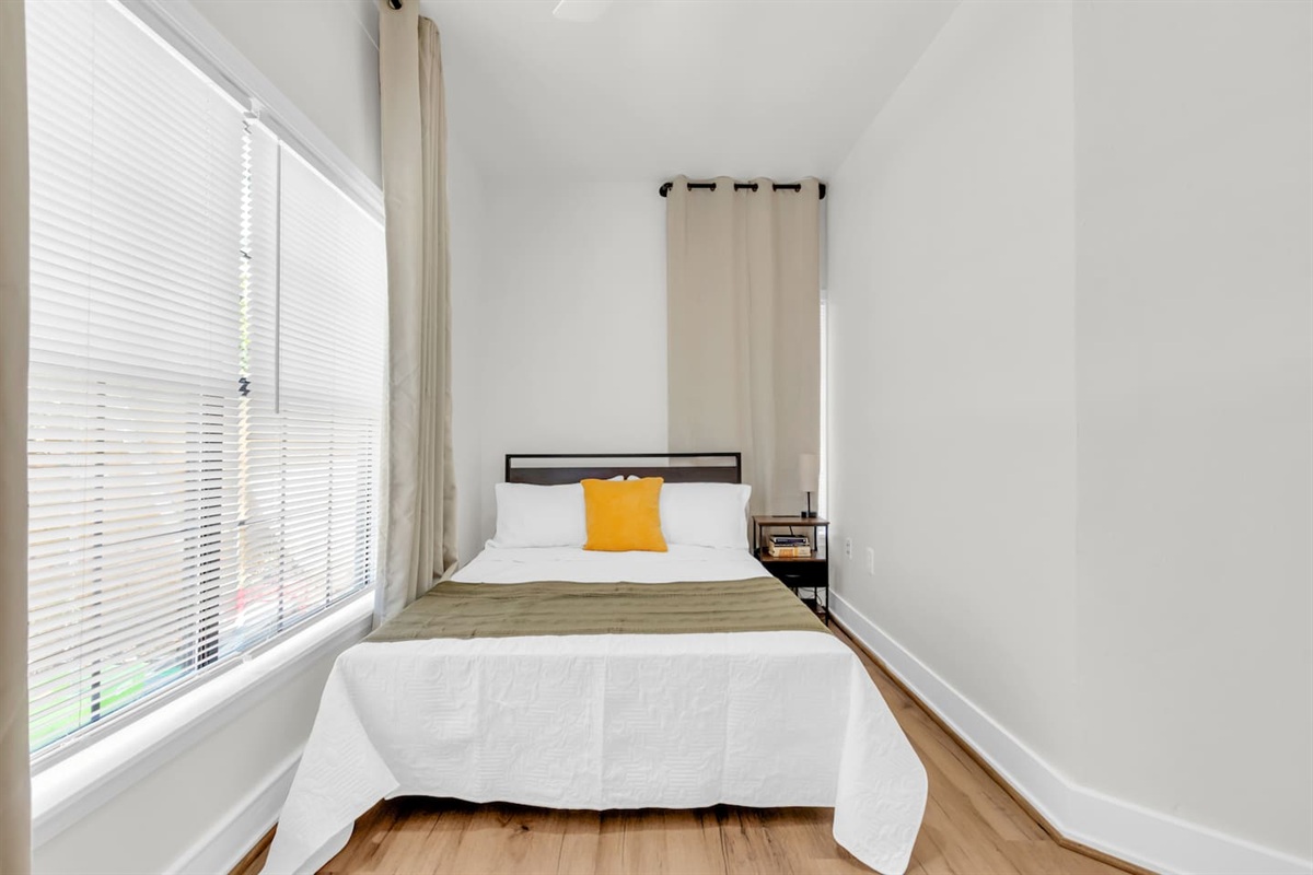 Bedroom with cozy queen bed, room darkening shades, and fresh decor.