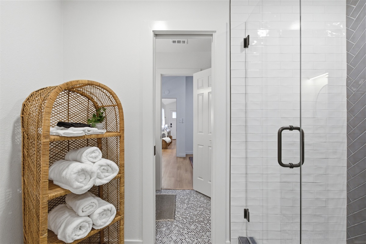 Fresh towels, woven storage tower, and standing shower with glass door. Each bathroom stocked with Ginger Lily Farms essentials for every guest.
