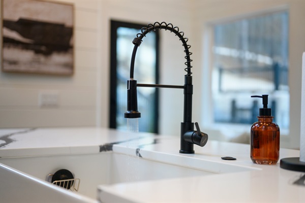 The oversized farmhouse sink with sleek black faucet makes cleanup easy while you enjoy peaceful forest views through the surrounding windows.