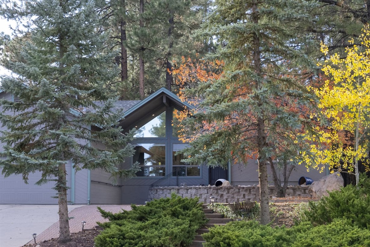 Home entrance with paved courtyard, mature trees, and natural stone details.