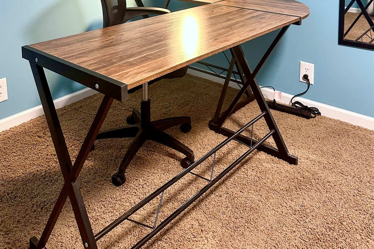 Lower-level office workspace featuring a desk, desk lamp, writing tools, notepad, and a conveniently placed power strip. Ideal for remote work, studying, or a quiet semi-private work zone.