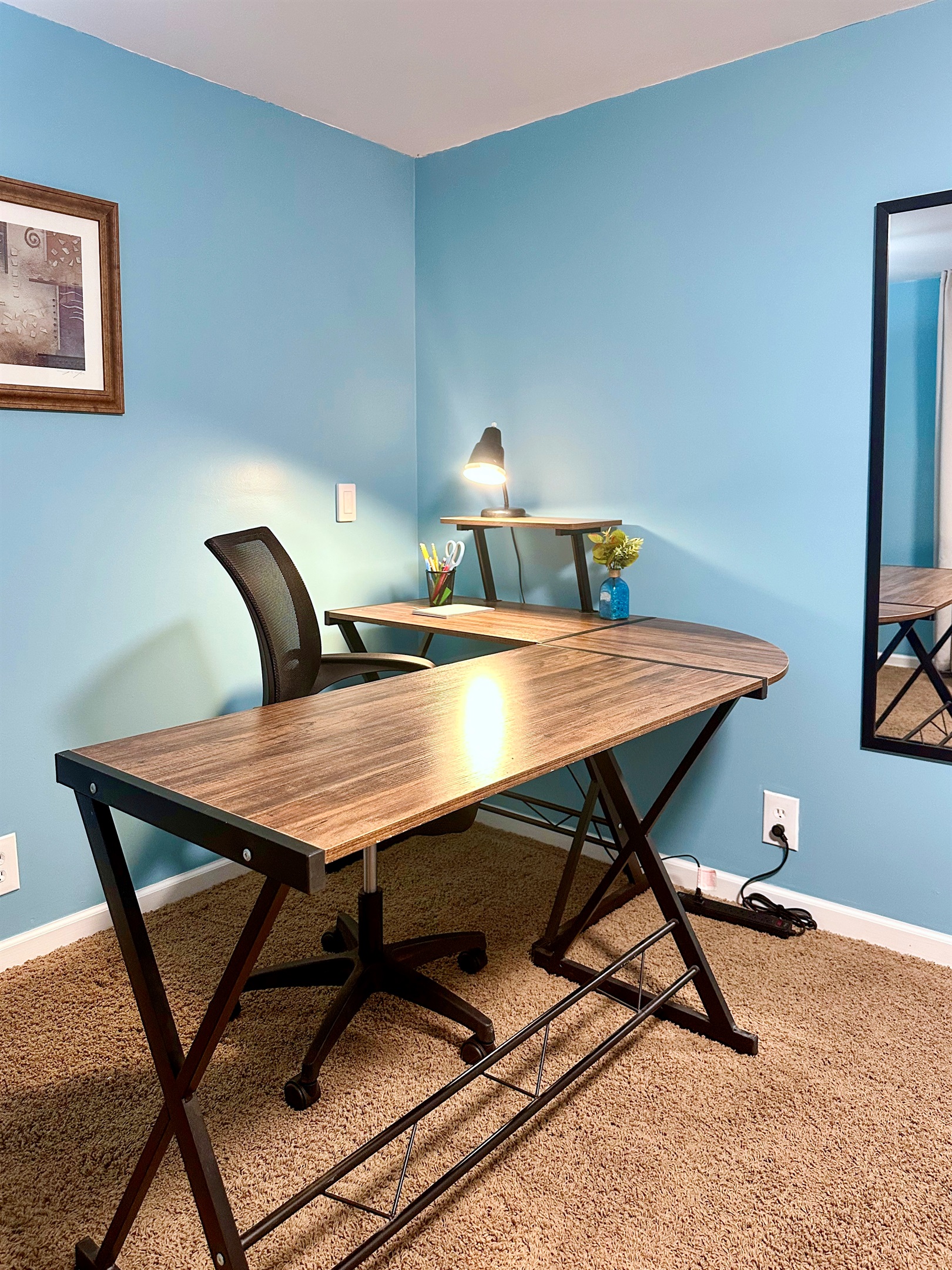 Lower-level office workspace featuring a desk, desk lamp, writing tools, notepad, and a conveniently placed power strip. Ideal for remote work, studying, or a quiet semi-private work zone.