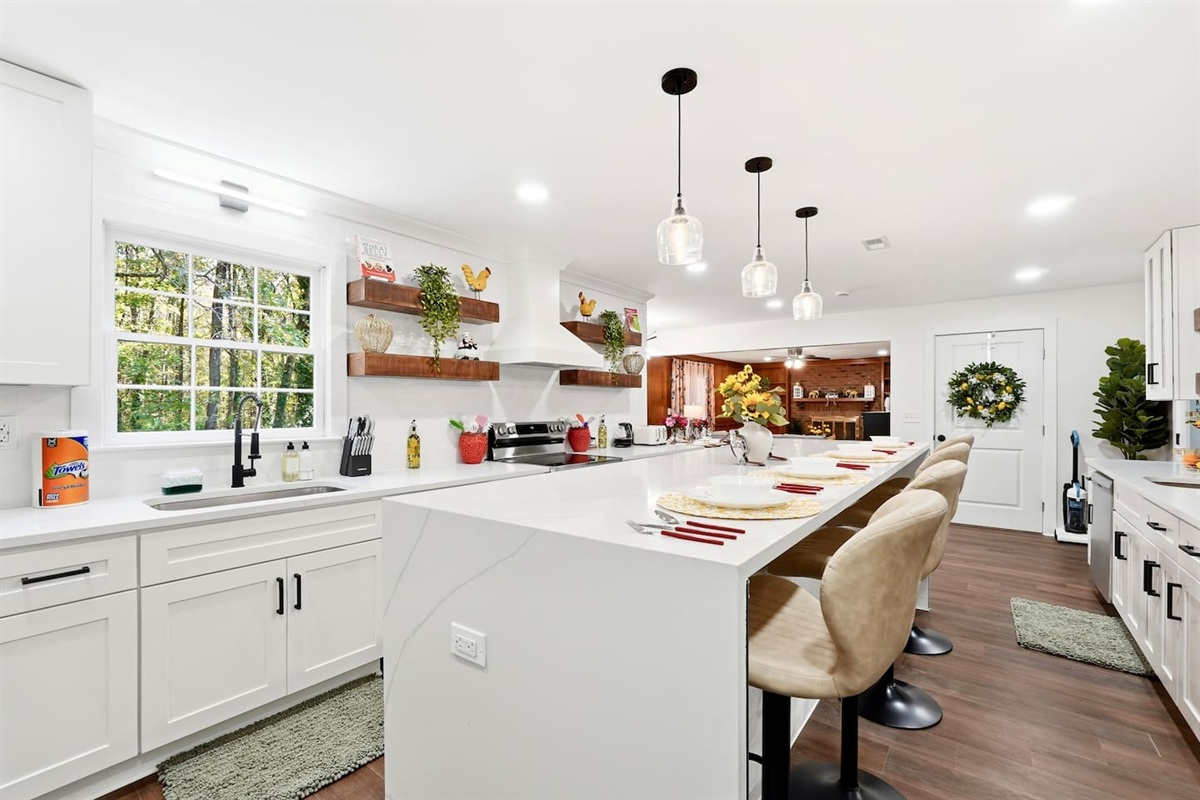 Beautiful white kitchen fully equipped with all the appliances and essentials of a home away from home. It also features a spacious island with stylish bar chairs, perfect for casual dining, morning coffee, or gathering while cooking.