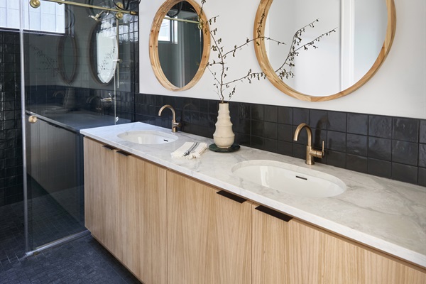 One of four stylish en-suite bathrooms, featuring dual vanities, bold black tile, and brass fixtures for a spa-like retreat.