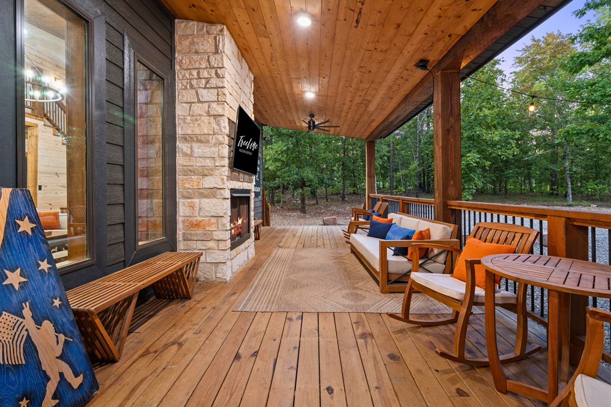 Relax on the covered deck with a stone fireplace and plenty of seating, surrounded by peaceful forest views.