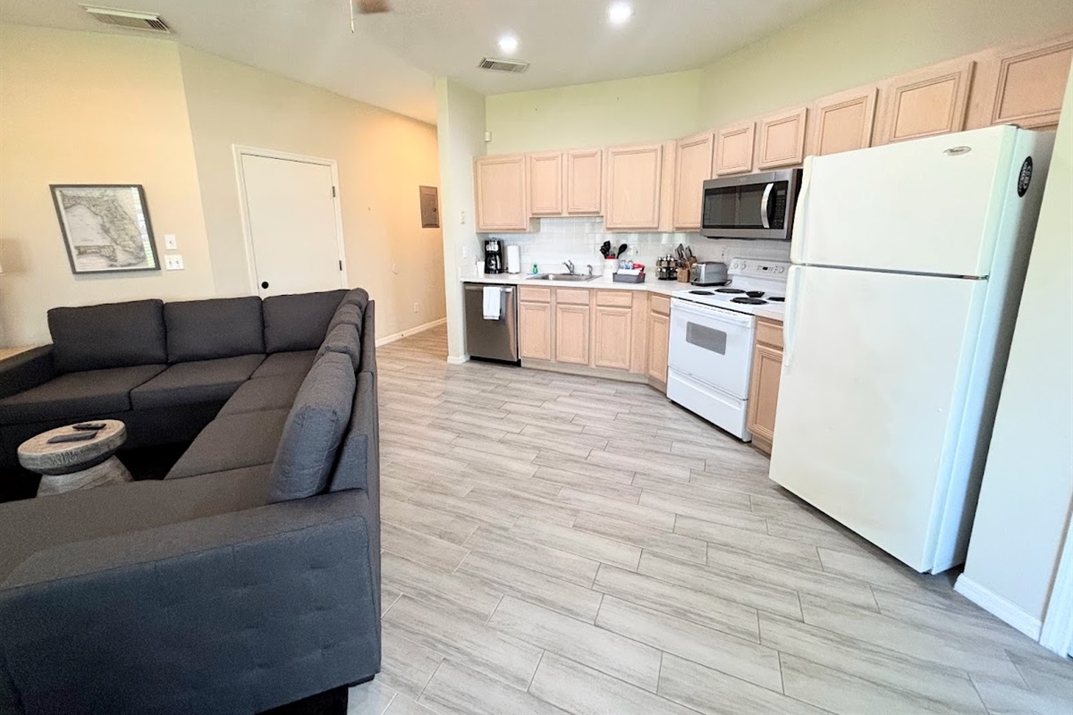 Open kitchen and living area with full-size appliances, wood-look flooring, and a comfortable sectional sofa.