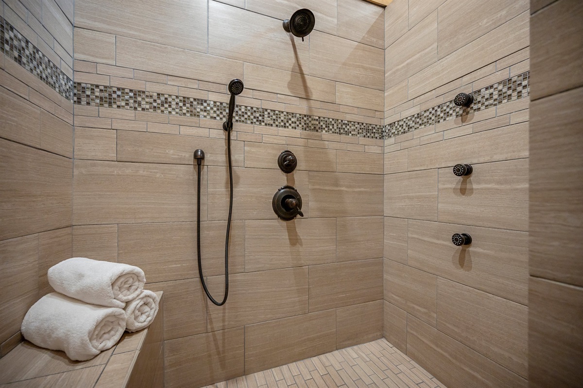 Walk in shower in the master bath has multi shower heads and bench seating.