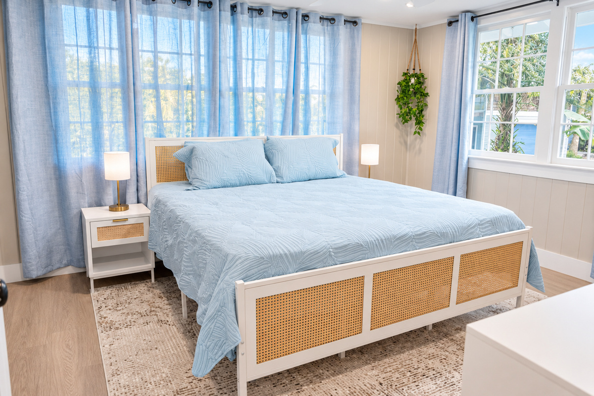Cozy bedroom with blue quilted bedding, rattan frame, warm lamps, and calming décor.